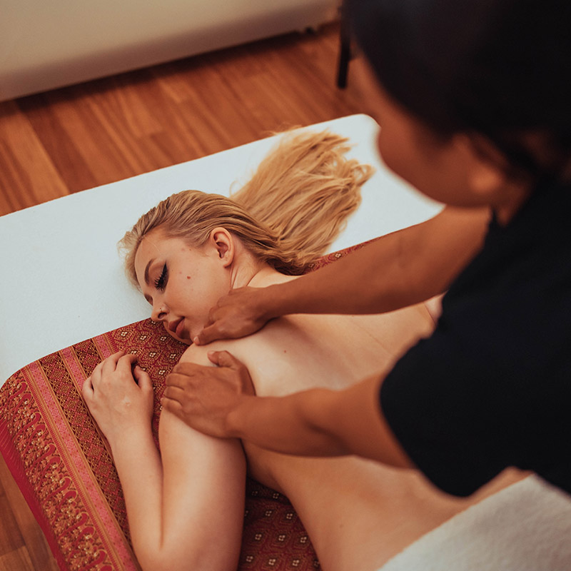 Uma mulher recebe uma massagem relaxante nas costas num tapete com padrões no salão Nattakan Thai Massage.