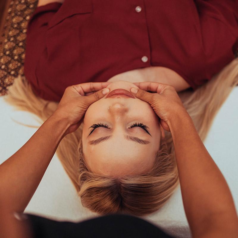 Person receiving a relaxing facial massage at Nattakan Thai Massage salon, lying down with eyes closed, while a therapist gently applies pressure to the sides of their jaw.