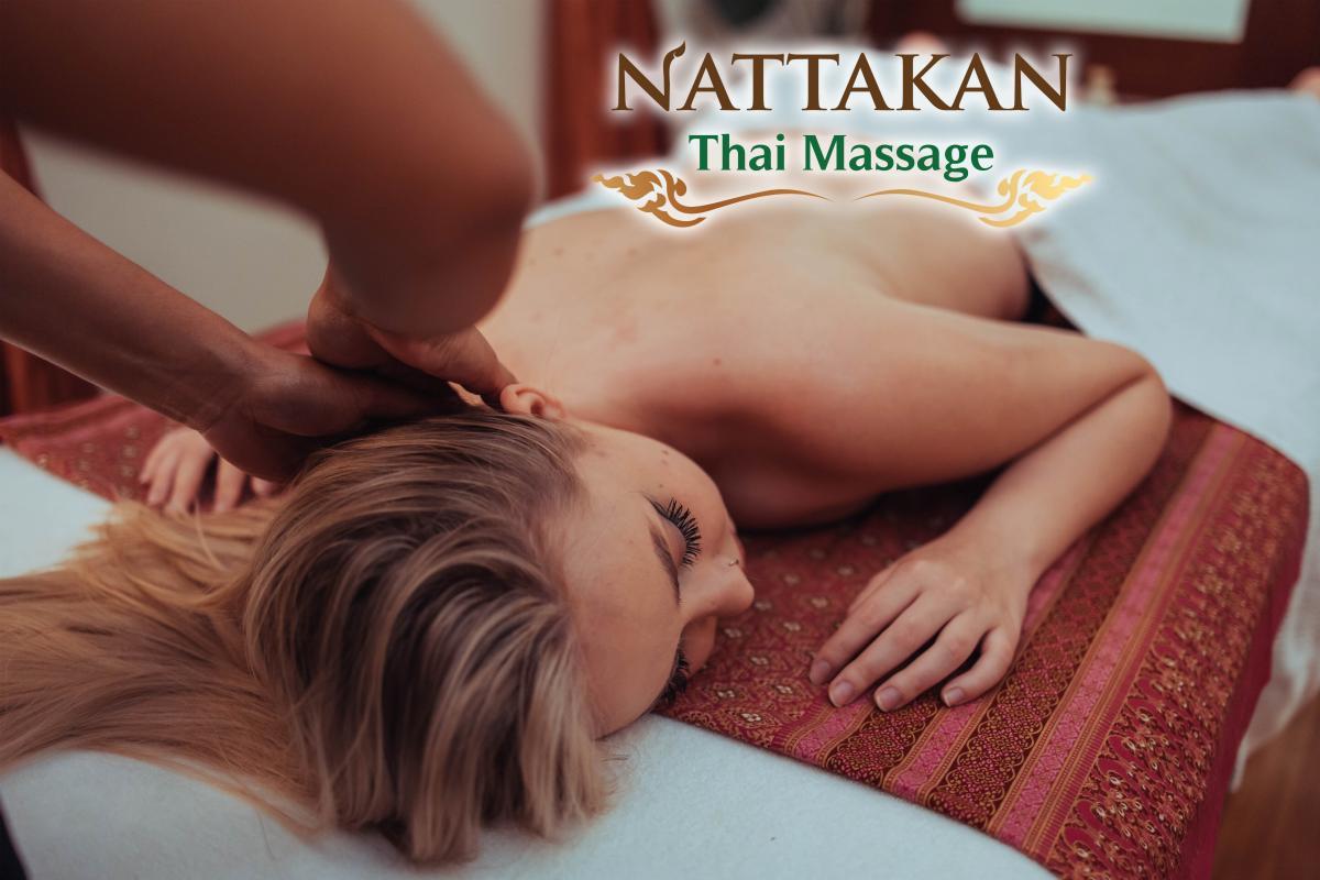 Klien menerima pijatan relaksasi di Nattakan Thai Massage dengan fokus pada area leher dan bahu. Klien berbaring di atas tempat tidur pijat bermotif merah dan emas yang indah, ditutupi dengan handuk putih.