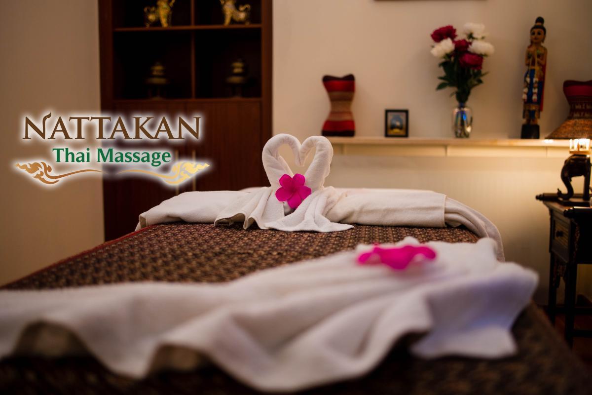 A serene room at Nattakan Thai Massage salon with a massage table adorned with white towels shaped into swans and decorated with pink flowers. The background features Thai decor, including traditional statues, a vase of flowers, and a calming atmosphere.