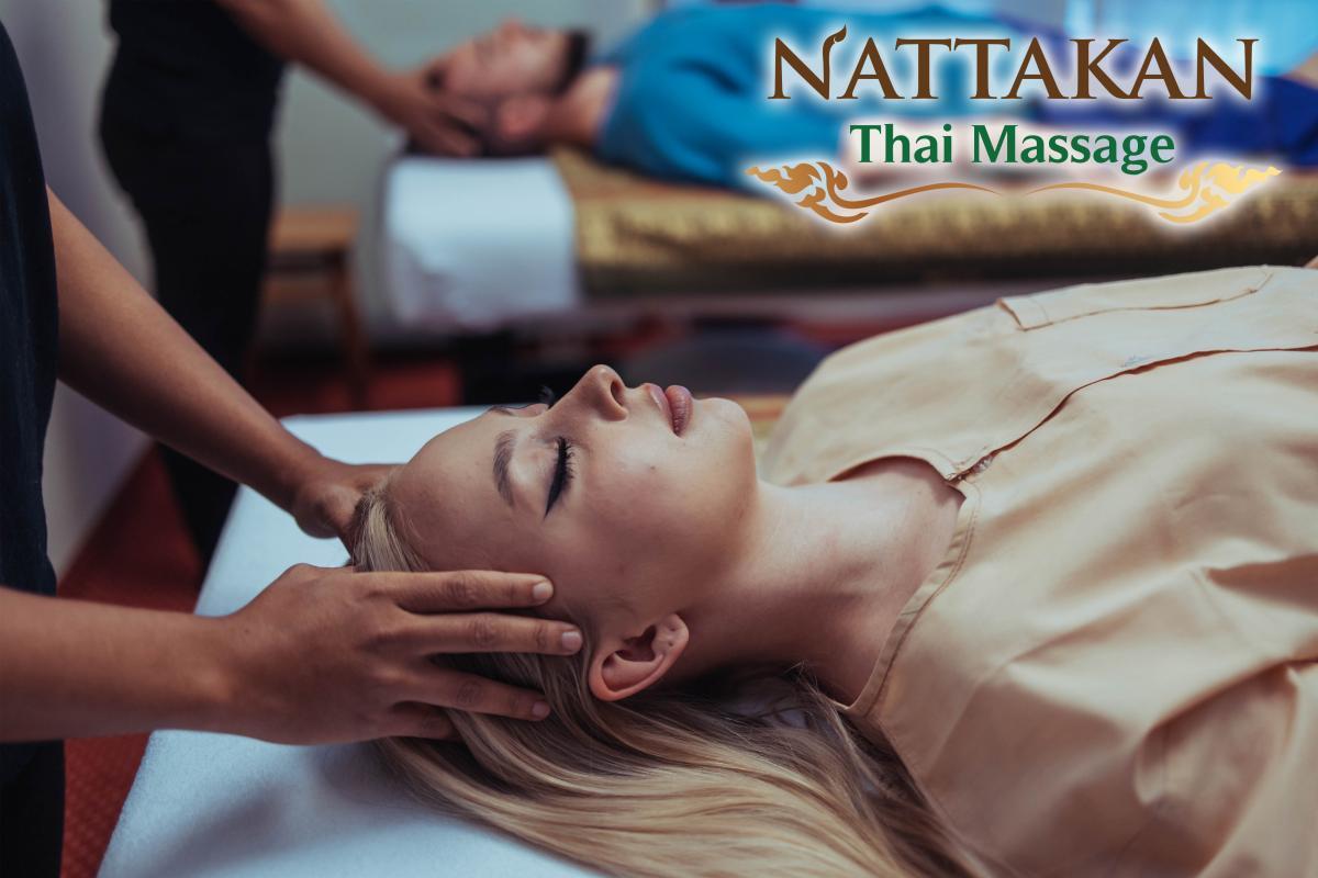 Uma pessoa a receber uma massagem relaxante à cabeça na Nattakan Thai Massage. Outra pessoa está a receber um tratamento semelhante em segundo plano. O logótipo da Nattakan Thai Massage é visível no canto superior direito da imagem.