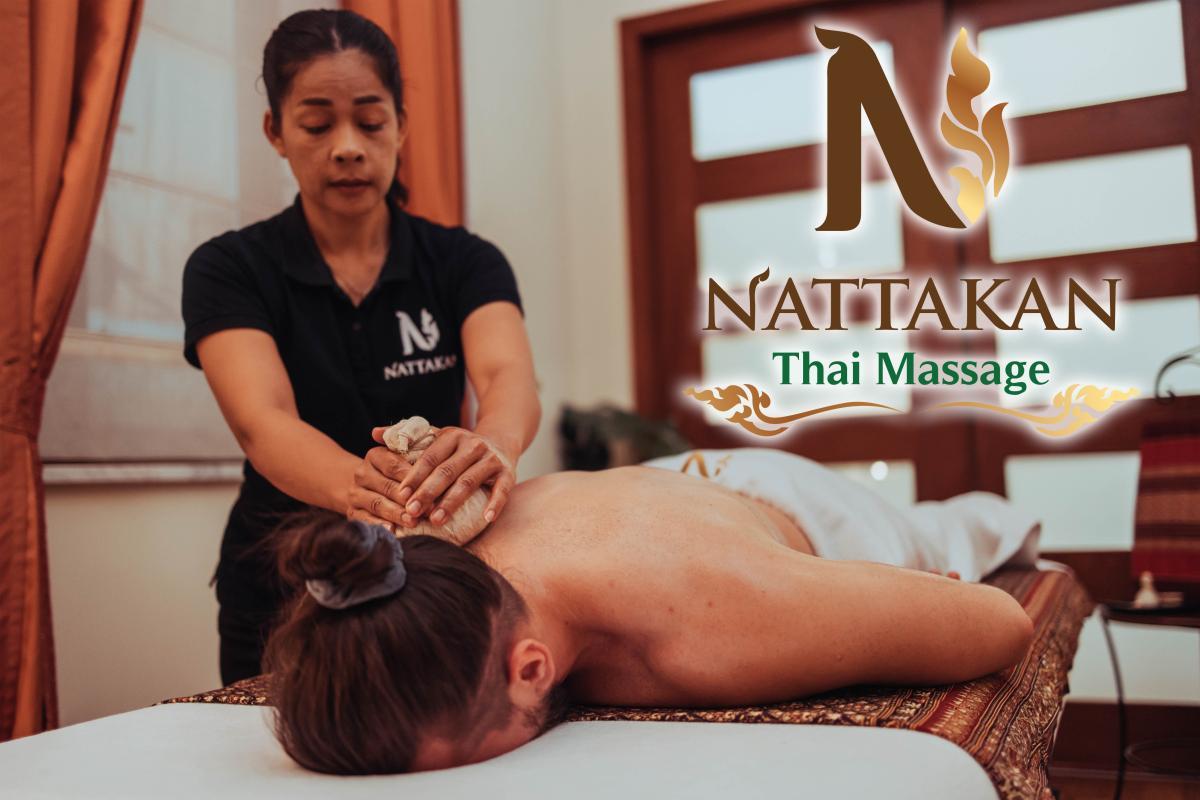 Therapeut voert een traditionele Thaise massage uit met kruidenkompressen op de rug van een klant bij Nattakan Thai Massage salon, logo op de achtergrond.