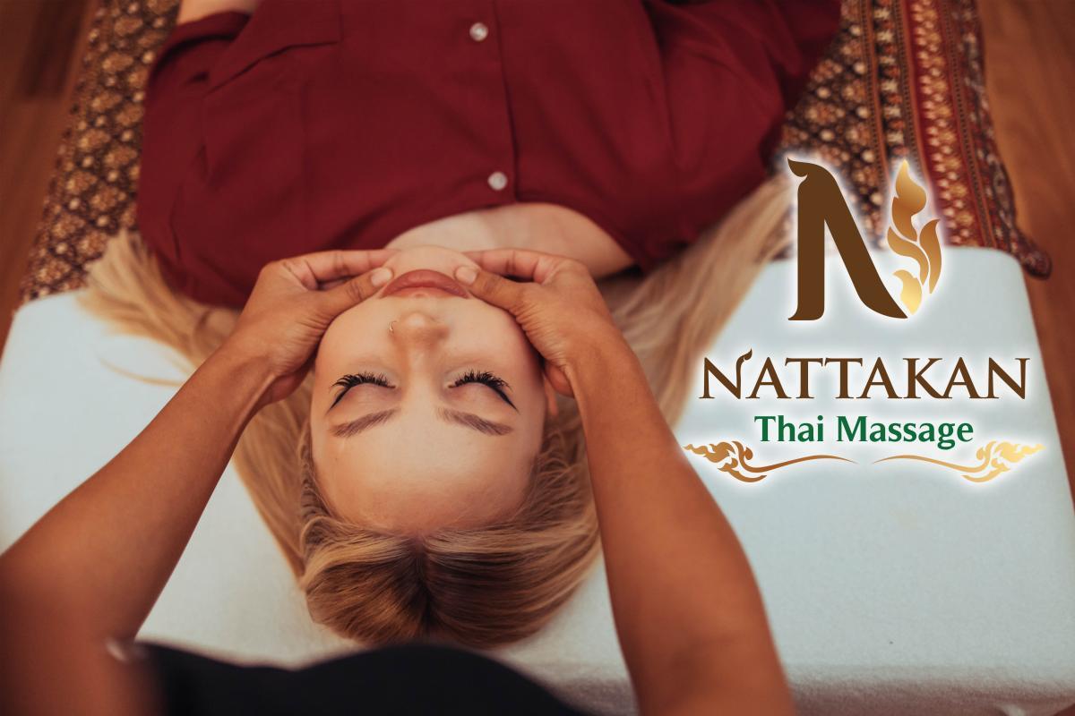 En person i rödbrun topp får ansiktsmassage liggande på en massagebänk med Nattakan Thai Massages logotyp synlig till höger i bild.