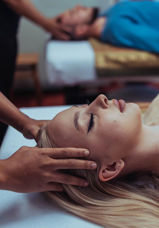 Close-up of a woman receiving a relaxing head massage at Nattakan Thai Massage salon, with another person in the background also receiving a massage.