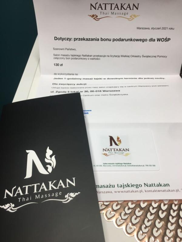 Afbeelding van documentatie over de cadeaubon van Nattakan Thai Massage, waaronder een bonkaart en een informatiefolder. De folder heeft de kop met het logo van Nattakan Thai Massage en bevat details over de cadeaubon ter waarde van 130 PLN, geschonken voor de veiling van Wielka Orkiestra Świątecznej Pomocy. De folder legt verder uit dat de bon de drager recht geeft op een Thaise massagesessie van een uur bij Nattakan Thai Massage, gevestigd in ul. Zgoda 5 lokal nr 30, 00-018 Warschau. Op het zwarte boekje staat prominent het logo van Nattakan Thai Massage.